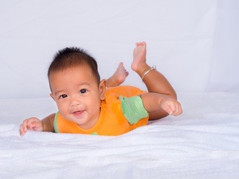 asian infant lie on the stomach, wearing an orange shirt on a white cloth.