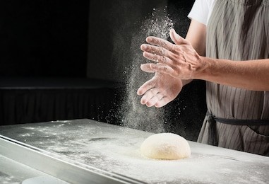 woman baker sprinkled flour on roll dough on a wooden board. process of preparing pizza. cooking time, cooking concept, selective focus