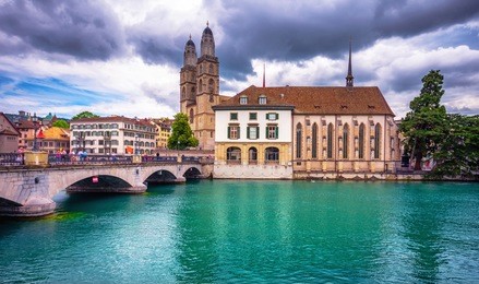 beautiful view of historic city center of zurich with famous fraumunster church and munsterbucke crossing river limmat on a sunny day with blue sky and clouds in summer, canton of zurich, switzerland