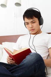 a young asian man reading a book on a bed