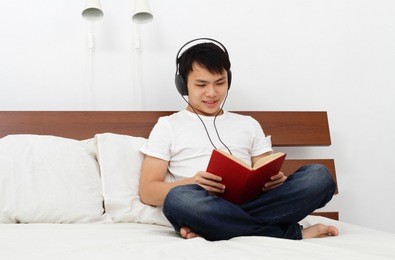 a young asian man reading a book on a bed