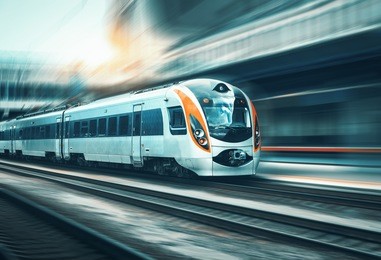 high speed train in motion at the railway station at sunset in europe. modern intercity train on the railway platform with motion blur effect. industrial landscape with passenger train on railroad