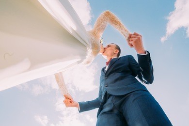 chherful newlyweds kissing with amazing blue sky as background. low angle shot