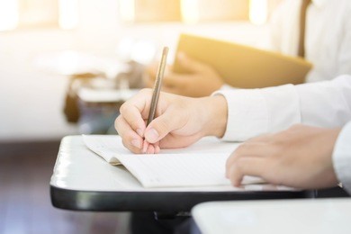 soft focus university or high school student holding pen.sitting on row chair taking final exam in examination room or study in classroom.student in uniform.education concept