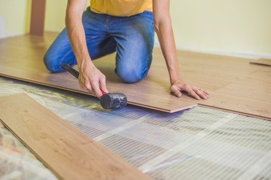 man installing new wooden laminate flooring on a warm film floor. infrared floor heating system under laminate floor