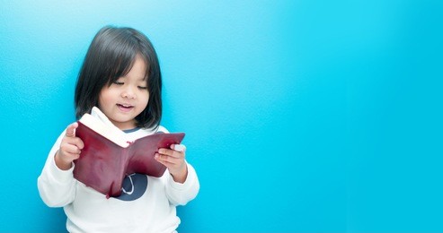 cute little asian girl in pajamas reading bible before sleep.hands holding on a holy bible in bed room concept for faith, spirituality and religion.blue background.