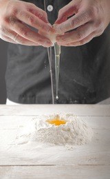 falling eggs into flour. hands breaking cracking a raw egg over flour, baking concept. baker kneads the dough for the pasta. the process of breaking eggs, food in motion. 