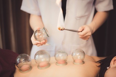 adult male physiotherapist is doing acupuncture on the back of a female patient. patient is lying down on a bed and is covered with royal blue towels.