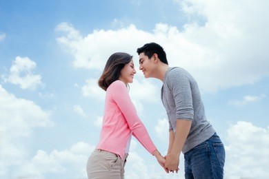 young beautiful asian woman and man laugh against the dark blue sky with clouds