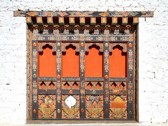 traditional  bhutanese style building decorated with carved wood window frames in paro rinpung dzong, buddhist monastery and fortress on a hill near the paro chu river. paro, bhutan.
