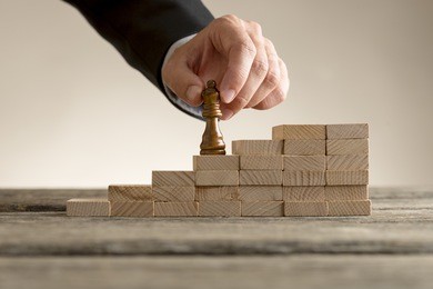business success and promotion concept with a businessman moving the queen piece up a series of steps formed by building blocks.