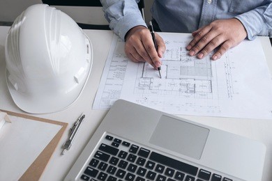 engineering or creative architect in construction project, engineers hands working on construction blueprint and building model at a workplace in office, building and architecture concept.