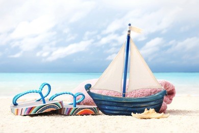 toy ship, flip-flops and towel on sand near sea. summer vacation concept