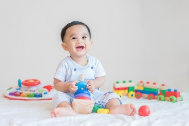 adorable asian baby boy 9 months sitting on bed and playing with color developmental toys at home.