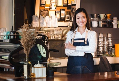 asian female barista wear jean apron crossed her arms at counter bar with smile face, cafe service concept, owner business start up.