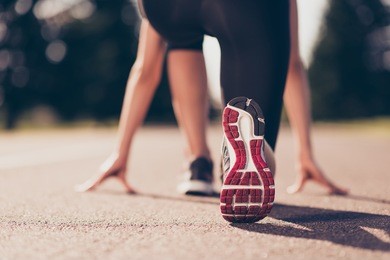 ready to go! close up cropped low angle photo of shoe of female athlete on the starting line of a stadium track, preparing for a run. sunny spring day
