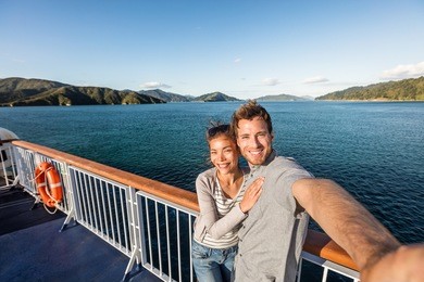 cruise couple tourists taking selfie on new zealand travel. people traveling on ferry boat marlborough sounds taking self-portrait picture with mobile phone smiling at camera.