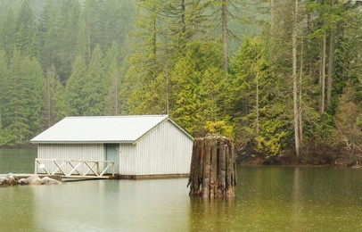 calm and peaceful lake with a wooden house and forest in background at rainy day