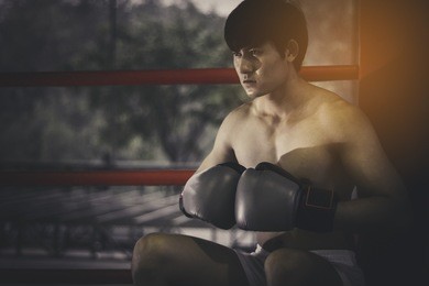 young asian boxer fighter sitting in the corner on sunset background, fight, workout, muscle, strength, power - the concept of strength training and boxing.