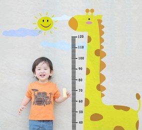 closeup happy asian kid stand for measure height with cute cartoon at the marble stone wall textured background