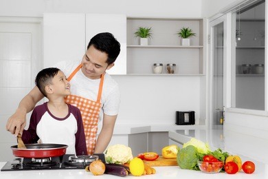portrait of a young man and his son cooking vegetable with a frying pan in the kitchen