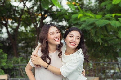 asian sisters hugging and smiling in the park.