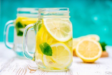 lemon water, lemonade in mugs with handles, mason jar on a white wooden table. cut lemons in the background.