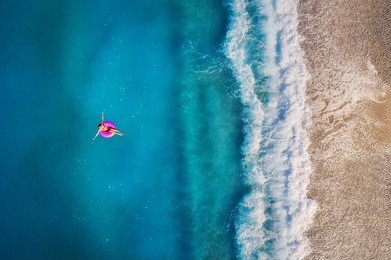 aerial view of young woman swimming on the pink swim ring in the transparent turquoise sea in oludeniz,turkey. summer seascape with girl, beautiful waves, azure water in sunny day. top view from drone