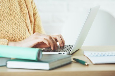 side view and close up of woman hands typing on laptop keyboard placed on wooden office desktop with supplies. technology concept 