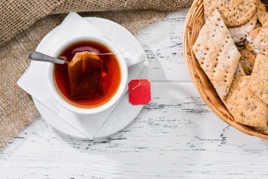 cup of tea and basket with cookies served for breakfast on wooden table, top view 