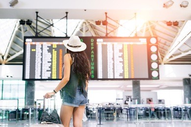 asian young hipster woman in international airport looking at the flight information board, checking her flight.unrecognizable back