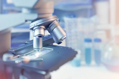scientific background with closeup on light microscope and laboratory out of focus. this image is toned. shallow dof, focus on the slide glass.