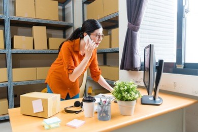 pretty attractive business woman using mobile cell phone calling and looking at computer checking online shopping order list.