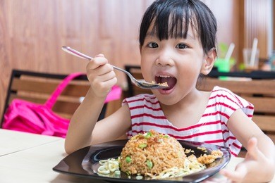 asian chinese little girl eating fried rice at outdoor cafe