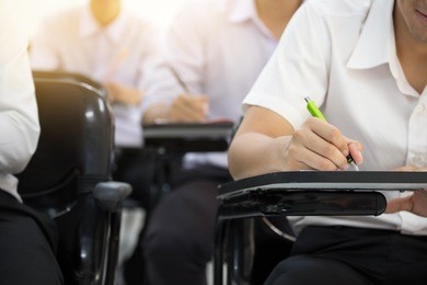 soft focus university or high school student holding pen.sitting on row chair taking final exam in examination room or study in classroom.student in uniform.education concept