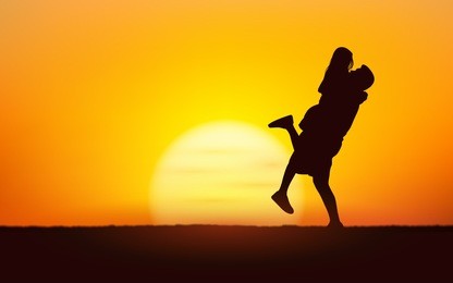 silhouette couple man lifting woman up in his arm under sunset sky background