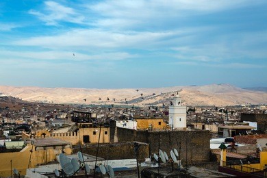 rooftops of old town with minaret and sand dunes in background in cloudy evening. fes el bali (medina), fez, morocco, north africa.