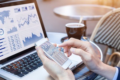 close-up of hands of person analyzing stock market chart and key performance indicators (kpi) with business intelligence (bi) on notebook computer and smartphone screen, fintech (financial technology)