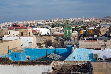 rooftops of old town with decorated minaret in cloudy evening. fes el bali (medina), fez, morocco, north africa.