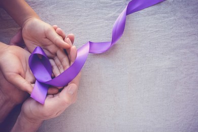 hands holding purple ribbons, toning copy space background, alzheimer disease, pancreatic cancer, epilepsy awareness, domestic violence awareness 