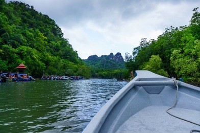 in boat shot during the river cruise showing the tree covered hills, cloudy skies and beautiful green water in in kilim park langkawi. this is a popular tourist destination