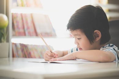 little asian child  using a pencil to write on notebook at the desk
