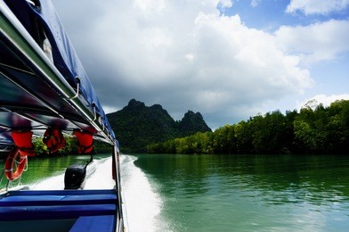 boat moving at high speed on a beautiful river in langkawi, shot from inside the boat. the seating, safety jackets and outboard motor are visible as are the beautiful tree covered hills, cloudy skies