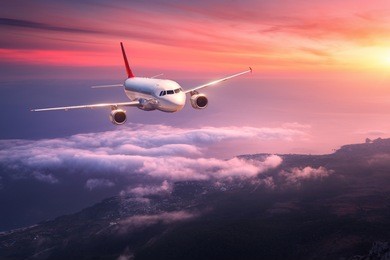 passenger airplane. landscape with big white airplane is flying in the red sky over the clouds and sea at colorful sunset. passenger aircraft is landing at dusk. business trip. commercial plane.travel