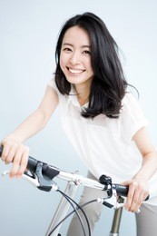 beautiful young woman on bicycle against light blue background.