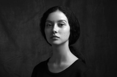 dramatic black and white portrait of a beautiful lonely girl with freckles isolated on a dark background in studio shot