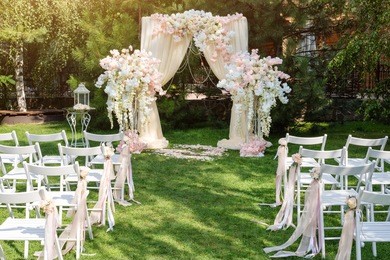 wedding arch decorated with cloth and flowers outdoors. beautiful wedding set up. wedding ceremony on green lawn in the garden. part of the festive decor, floral arrangement.