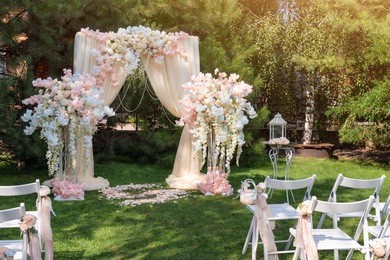 wedding arch decorated with cloth and flowers outdoors. beautiful wedding set up. wedding ceremony on green lawn in the garden. part of the festive decor, floral arrangement.