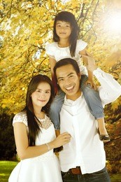 young parents with her daughter smiling at the camera while playing together in the park, shot at autumn time
