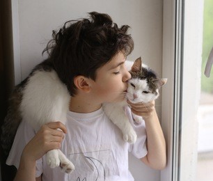 teenager boy with cat kissing look out of the window close up portriait